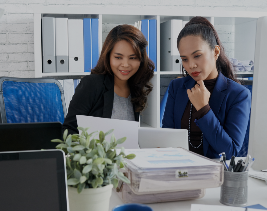 two-asian-female-colleagues-sitting-together-office-looking-document 1